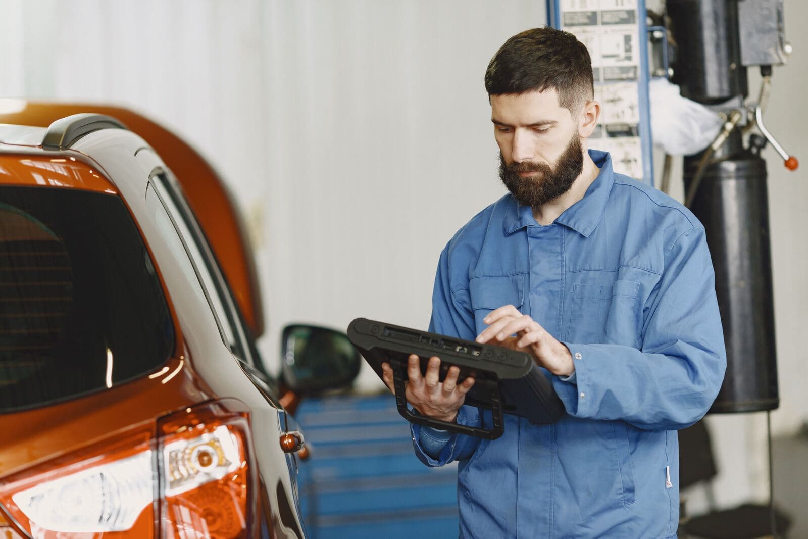 Technician reading a diagnostic tablet next to a car
